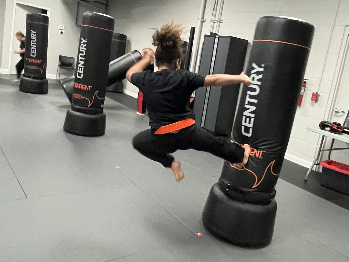 A Guardian Kids student throwing a flying kick into a heavy bag at Family First Spring Hill